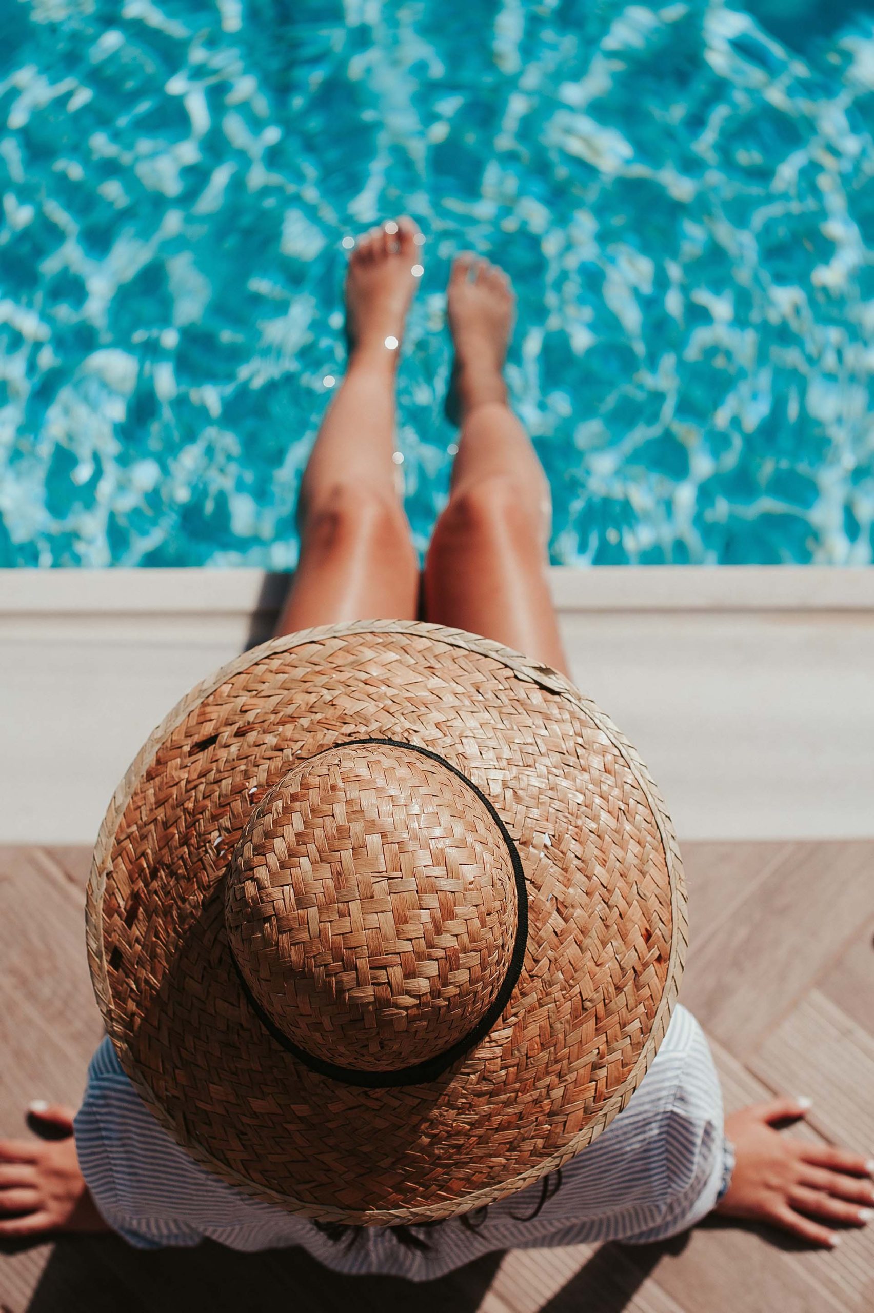 woman sitting on the side of a pool wearing a sun hat