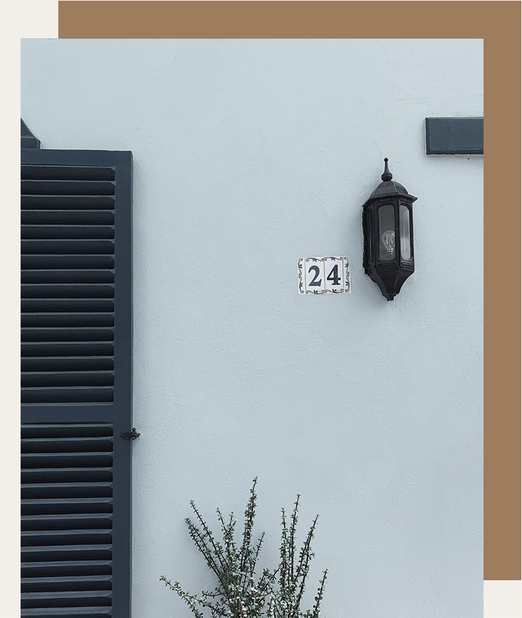 the front of a blue house with address numbers on the wall next to a sconce
